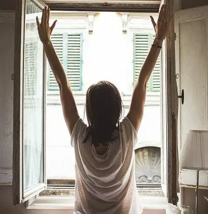 A woman raising her arms out of an open window.