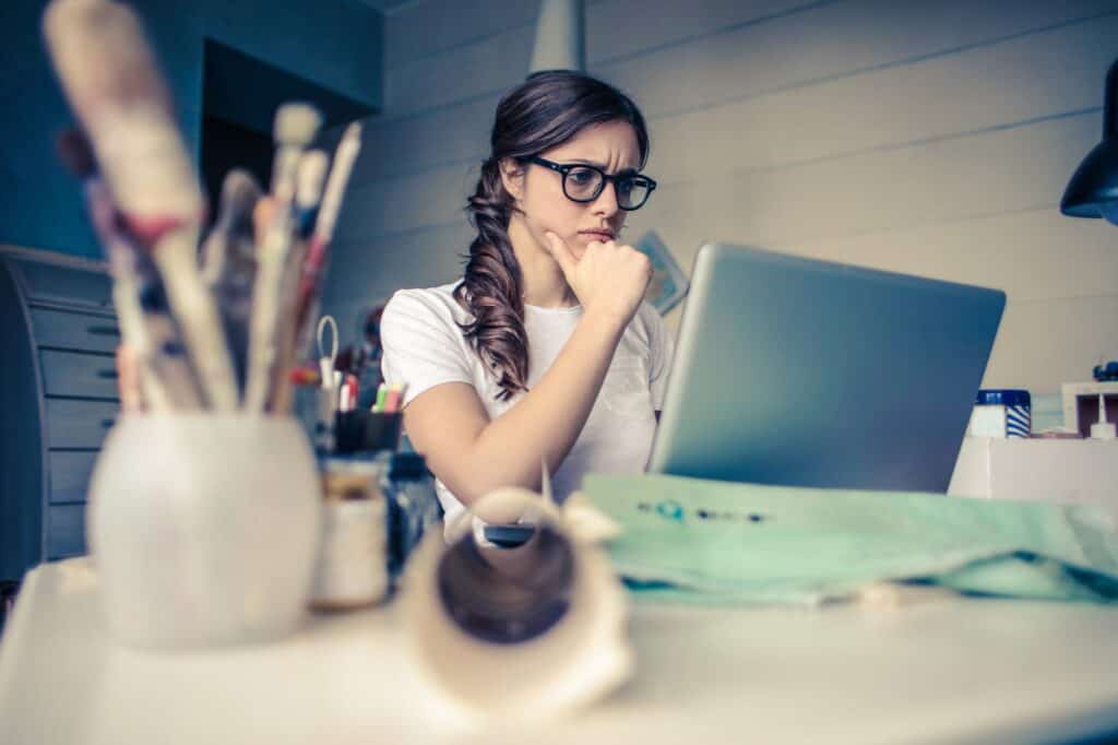 how to organize your work day - photo of a woman thinking about how to organize her work day woman in red top wearing black framed eyeglasses standing in front of white background 