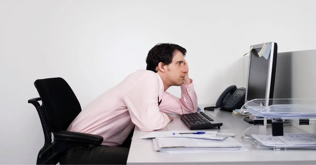 lower back pain after sitting too long -  a man sitting at his desk and slouching in front of the computer monitor