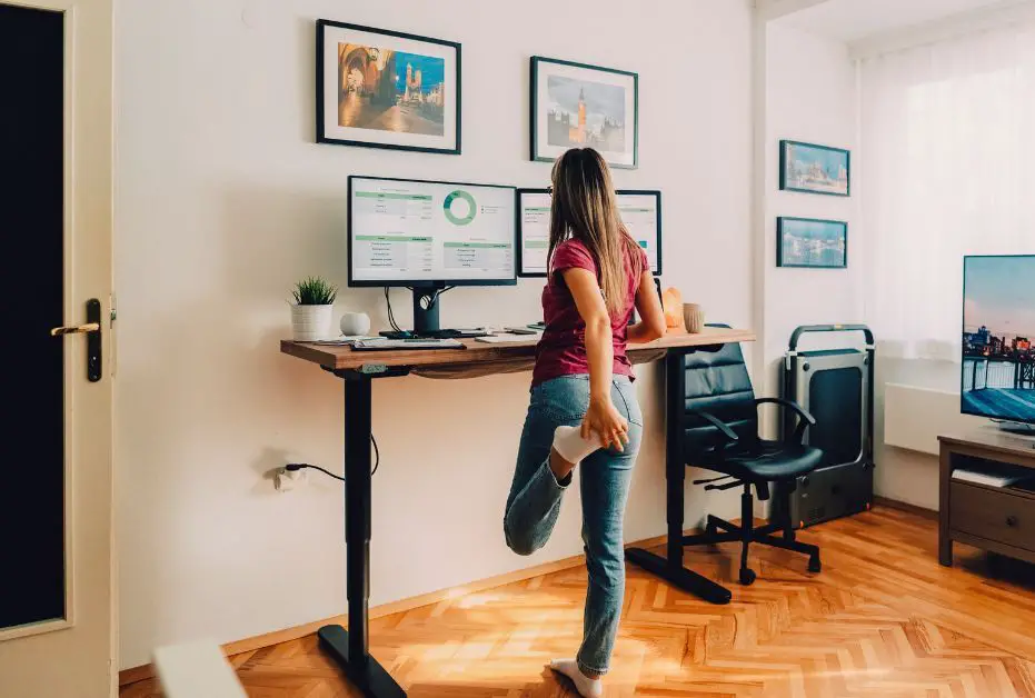 lower back pain after sitting too long -  a woman standing and stretching in front of her standing desk