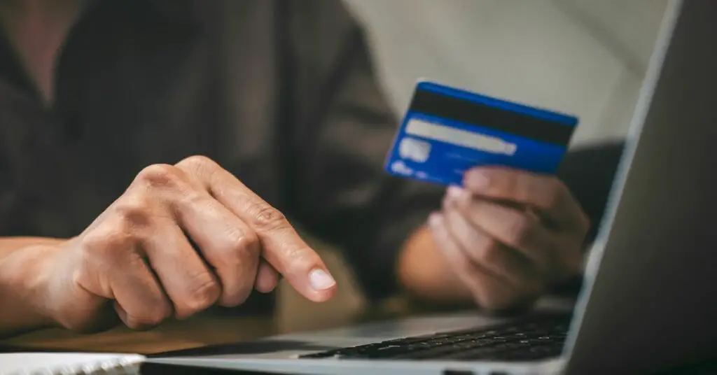 how to fight a chargeback - A person holding a credit card while typing on a laptop filing a chargeback.