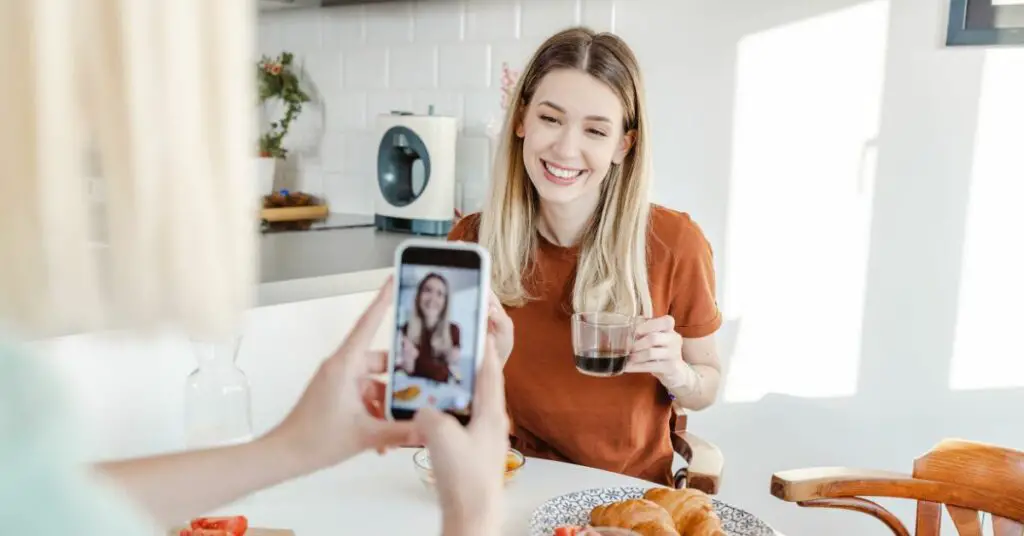 A woman is taking a photo with her phone while eating breakfast in order to generate online store promotion ideas.