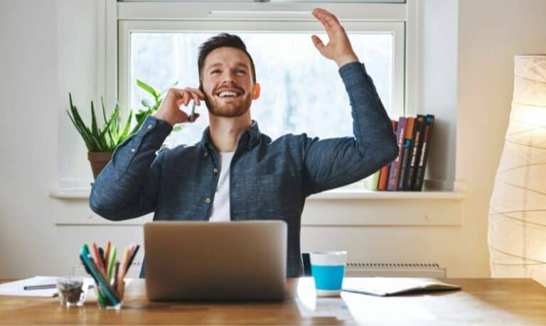 A man is effectively maintaining momentum at his desk while talking on the phone.