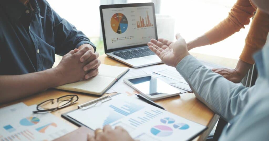 A group of people sitting around a table with laptops and graphs analyzing marketing performance.