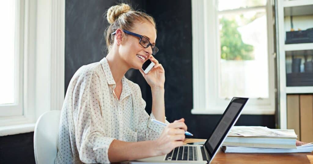 how to respond to negative reviews - A woman sitting at a desk and talking on the phone to follow up with the customer.