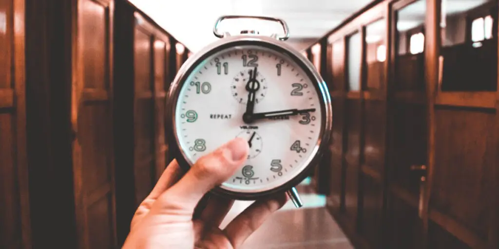 managing time effectively at work - A person effectively managing time at work by holding an alarm clock in a hallway.